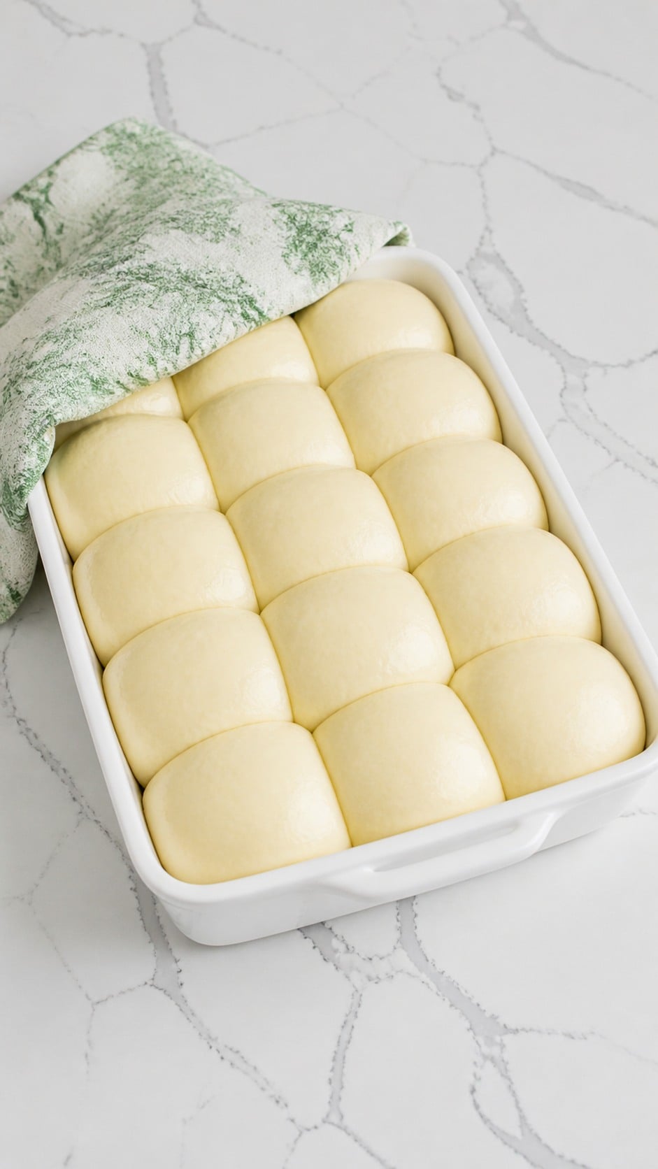 Puffy proofed yeast rolls beginning to touch in a white baking dish.