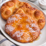 Indian fry bread with honey and powdered sugar on a white oval platter.