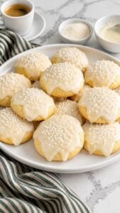 Italian Christmas cookies with white almond icing and nonpareils on a white platter.