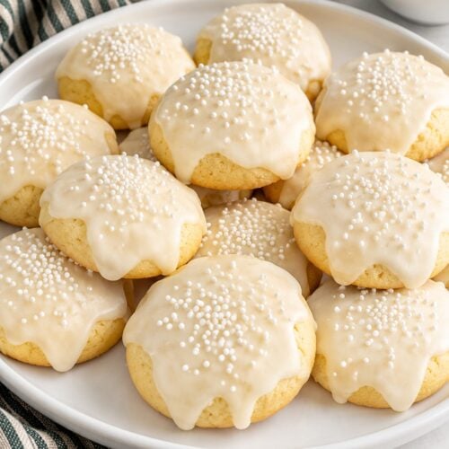 Italian Christmas cookies with white almond icing and nonpareils on a white platter.