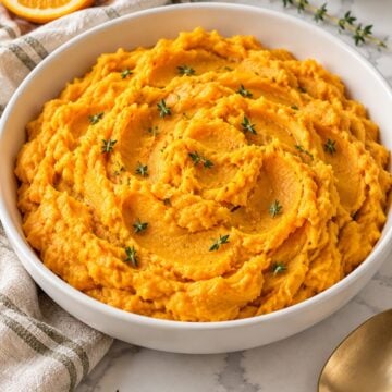 Mashed sweet potatoes with orange and thyme in a white serving bowl