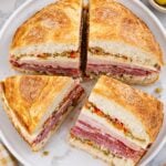 Muffuletta sandwich cut into four wedges on a white plate with layers of deli meats, cheese, and olive salad
