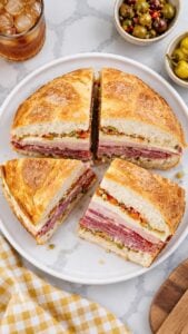 Muffuletta sandwich cut into four wedges on a white plate with layers of deli meats, cheese, and olive salad