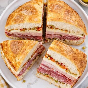 Muffuletta sandwich cut into four wedges on a white plate with layers of deli meats, cheese, and olive salad