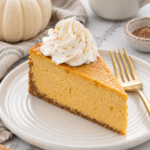 Pumpkin cheesecake slice with whipped cream and a light nutmeg dusting on an ivory plate.
