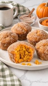 Pumpkin donut muffins with cinnamon sugar on an ivory platter, with orange crumb visible