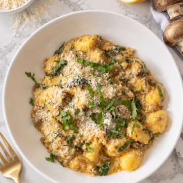 Overhead view of creamy pumpkin sausage gnocchi with mushrooms in a white bowl.