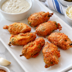 Golden fried scorpion tails with ranch dressing on a white rectangular platter.
