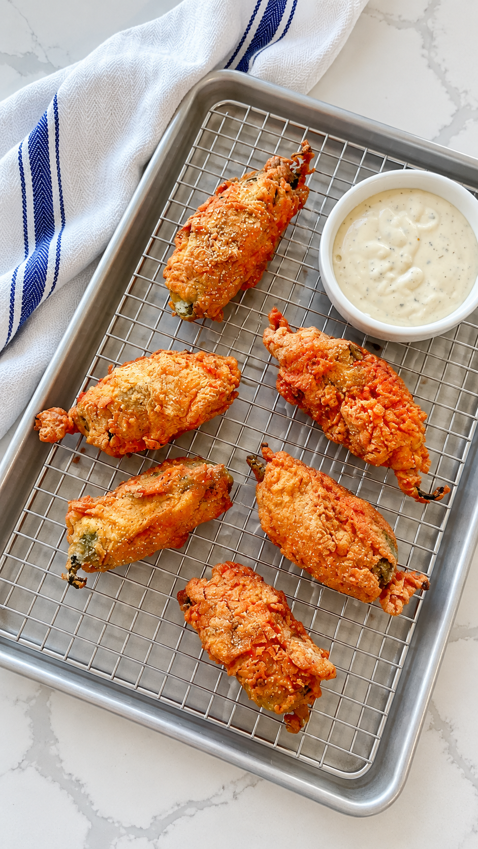 Golden fried scorpion tails draining on a wire rack over a baking sheet.