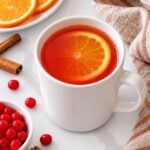Finished Red Hots apple cider served in a white mug with a fresh orange slice.