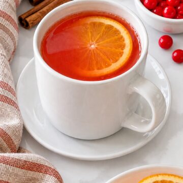 Red Hots apple cider in a white ceramic mug with a fresh orange slice.