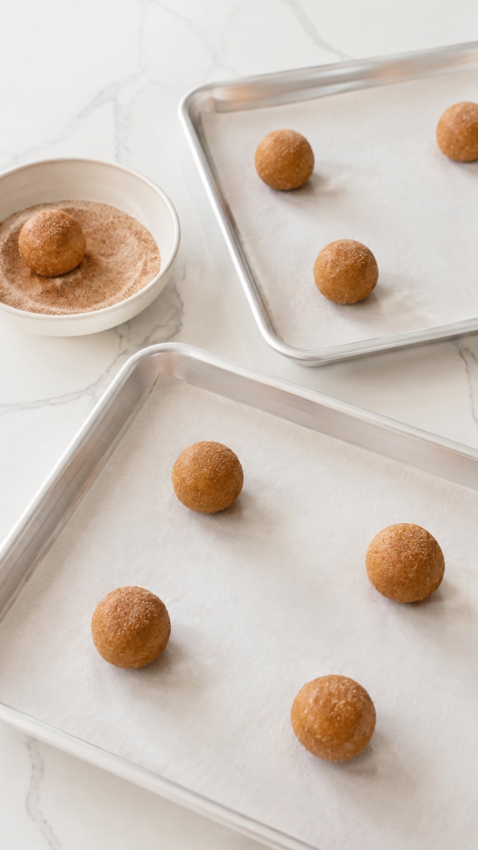 Pumpkin cookie dough balls rolled in spiced sugar and arranged on a lined baking sheet.