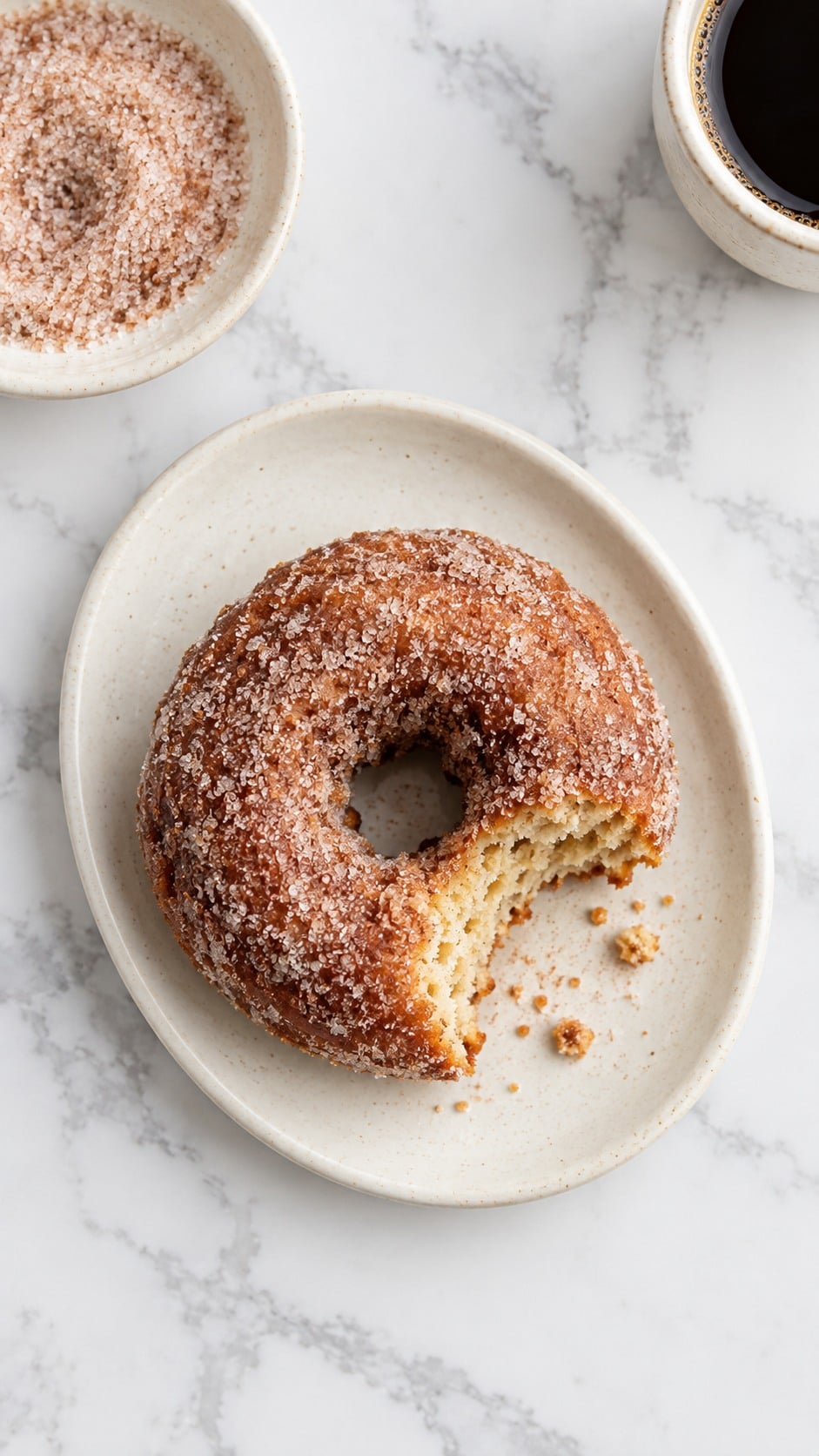 Overhead view of a bitten sour cream apple cider donut with coffee and cinnamon sugar.