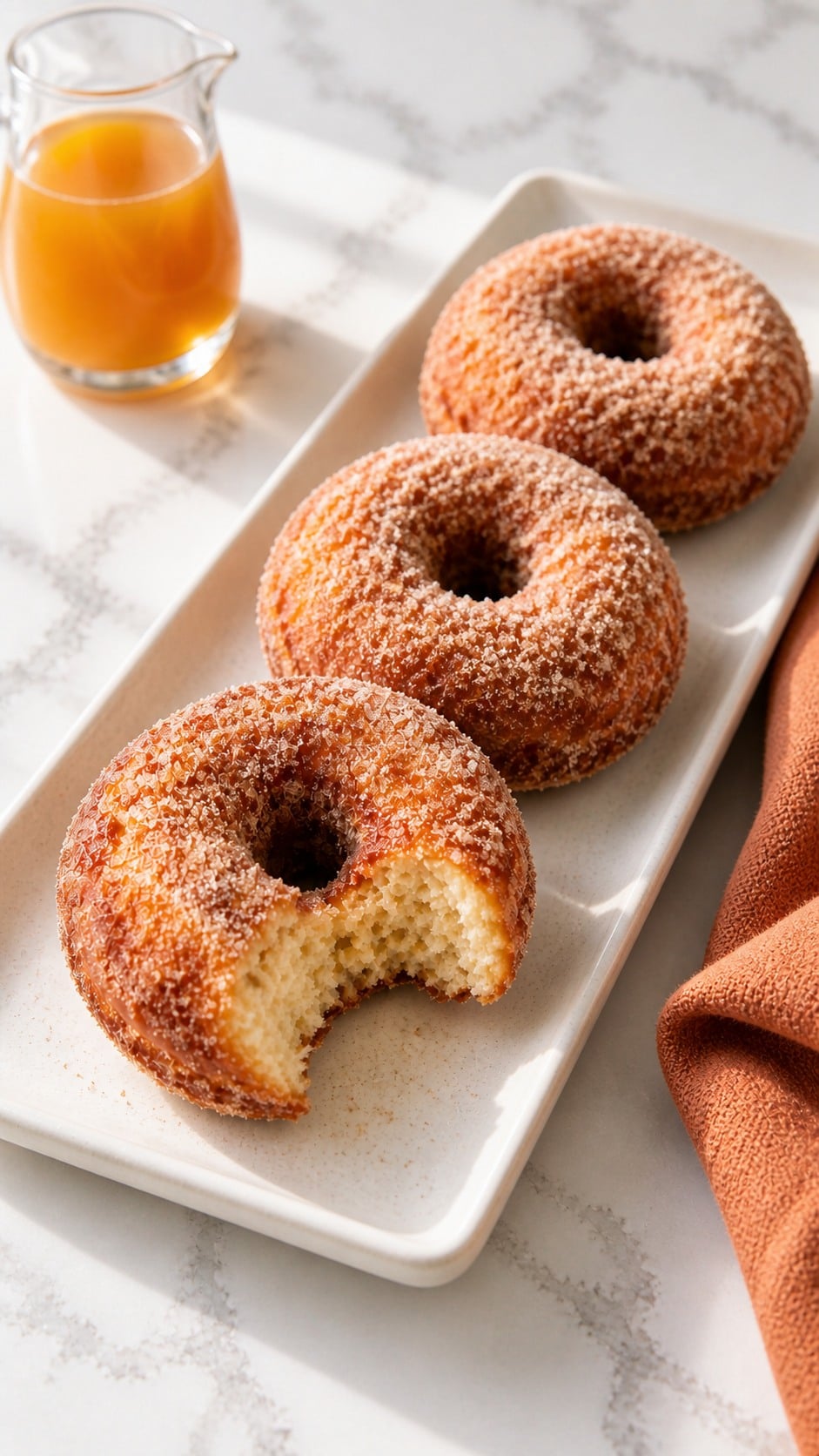 Three sour cream apple cider donuts on a rectangular tray with one bitten donut.