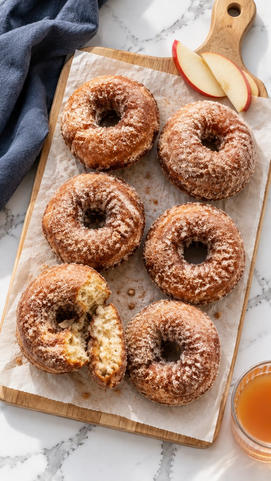 Sour cream apple cider donuts arranged on parchment with apple slices and cider.