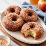 Cinnamon-sugar sour cream apple cider donuts arranged on an oval platter with apple cider.