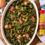 Southern collard greens and smoked ham in an ivory oval serving dish with Trappey's pepper sauce