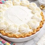 Stabilized whipped cream rosettes around a pie in a white dish.
