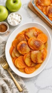 Sweet potato apple bake with tender slices in cinnamon-butter juices on a white plate