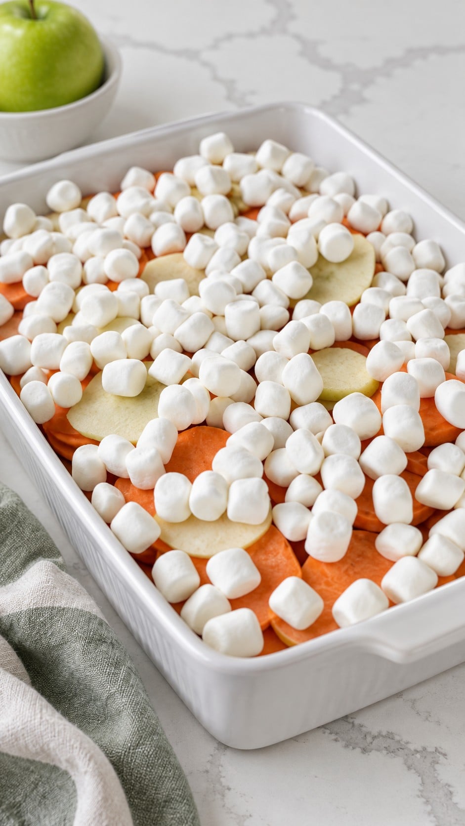 Raw sweet potato and apple layers topped with mini marshmallows in a baking dish