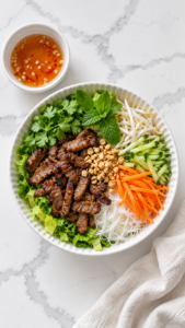 Assembled pork noodle bowl with cucumber, carrots, sprouts, herbs and peanuts