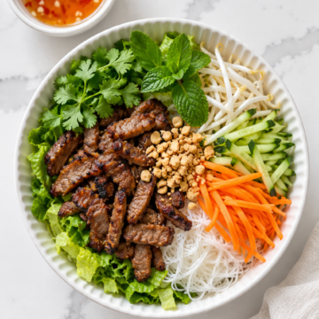 Assembled pork noodle bowl with cucumber, carrots, sprouts, herbs and peanuts