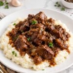Beef tips and brown onion gravy served over mashed potatoes on a plain white plate.