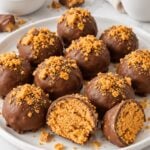 Milk chocolate coated Butterfinger balls with crushed candy topping and a cut center on a white plate.