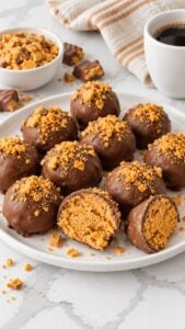 Milk chocolate coated Butterfinger balls with crushed candy topping and a cut center on a white plate.