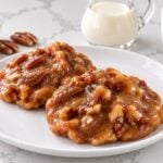 Chewy Texas pecan pralines with toasted pecan pieces in buttery caramel on a white plate.