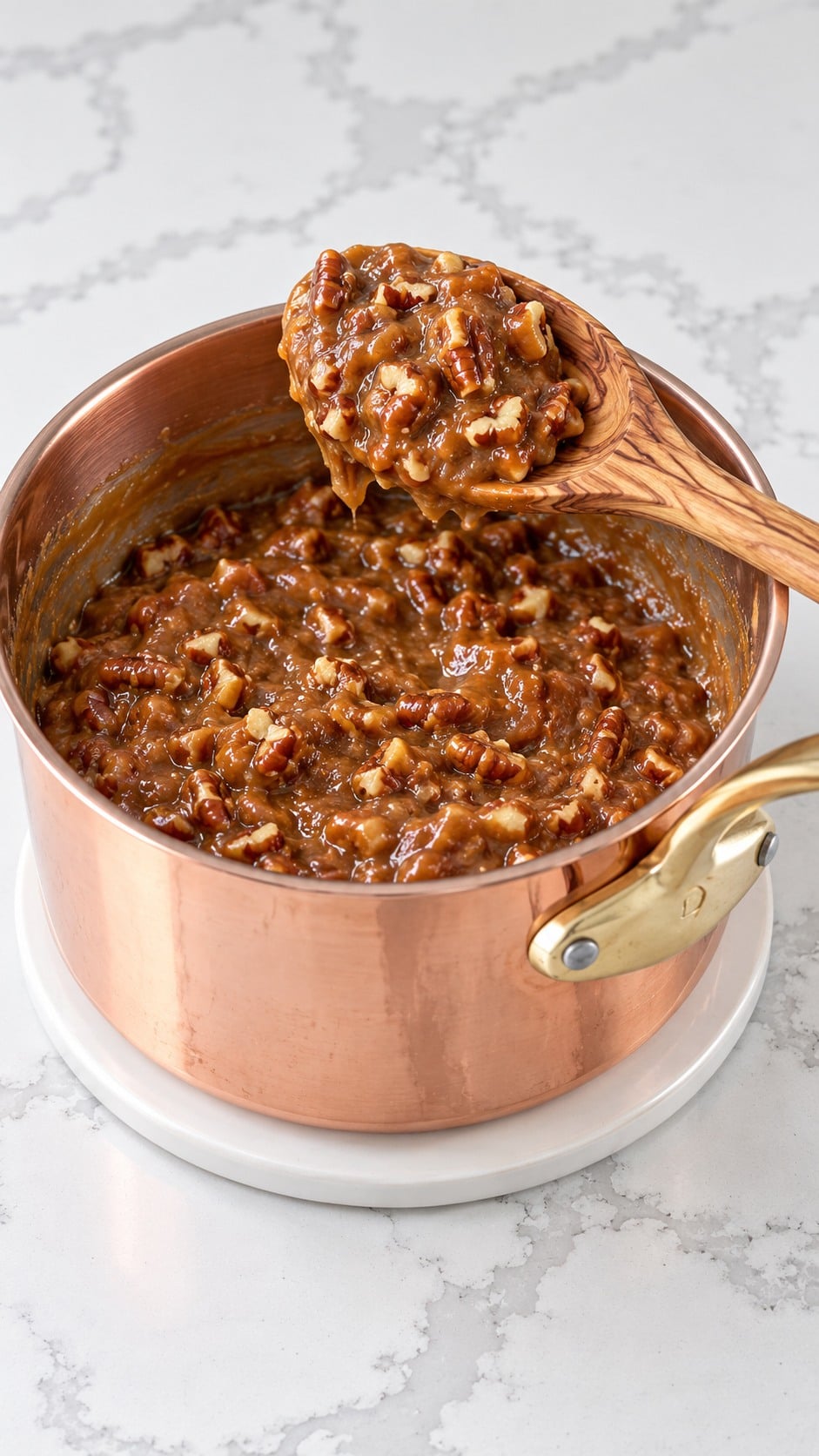 Toasted pecans mixed into thick caramel that holds a mound on a spoon.
