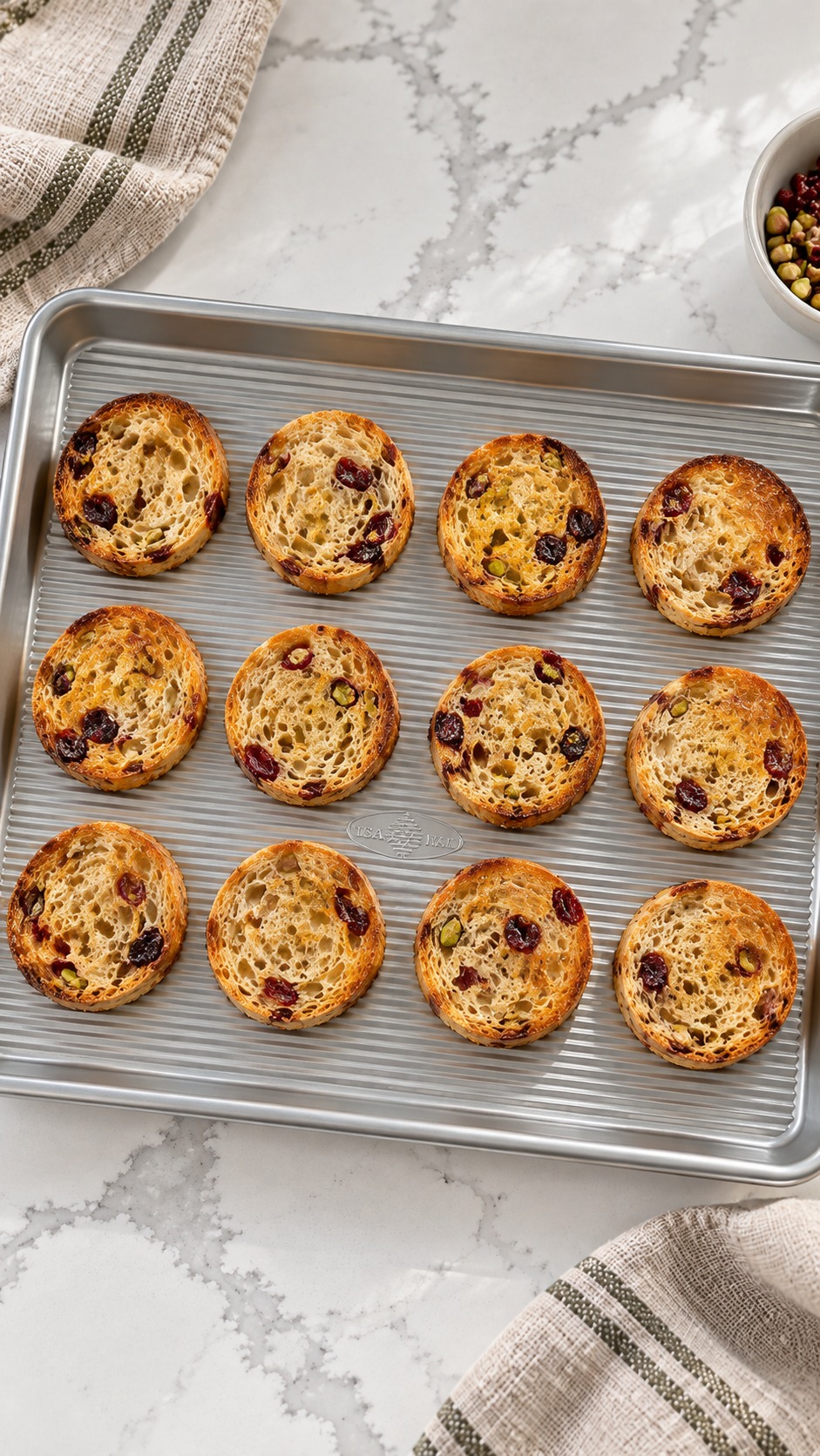Golden toasted cranberry-pistachio bread rounds on an unlined baking sheet.