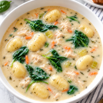 Creamy chicken and gnocchi soup with spinach in a white bowl.