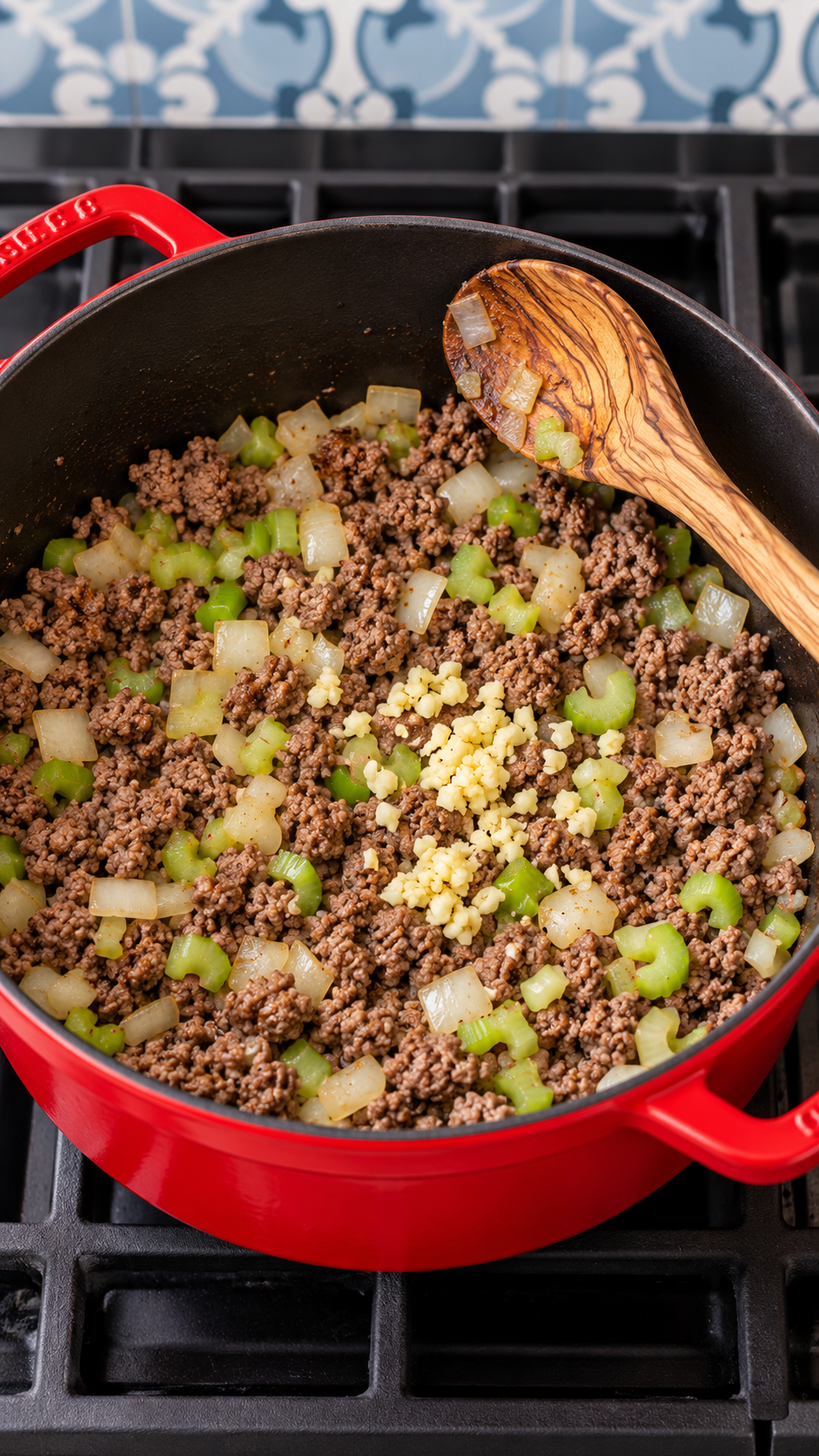 Ground beef browned with onion and celery in a red Dutch oven, with garlic added.