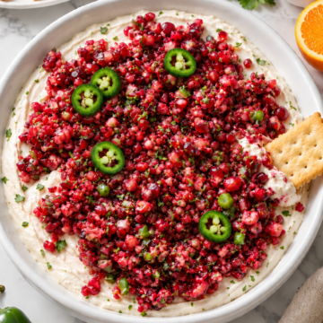Cranberry pomegranate jalapeño dip with cream cheese in a plain white ceramic dish and Club crackers.