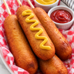 Homemade corn dogs with yellow mustard on a white oval platter.