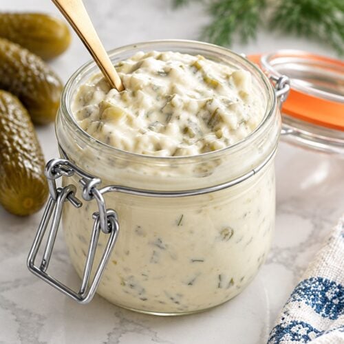 Chunky homemade tartar sauce in a glass jar with dill pickles, lemon, and fresh dill.