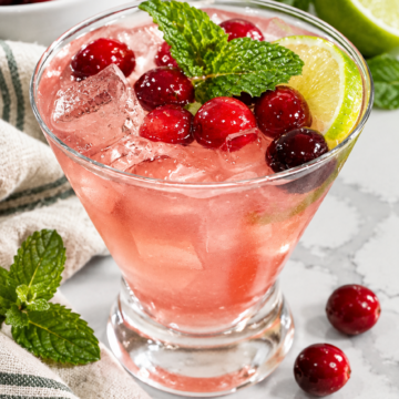 Pink Jingle Juice with cranberries, lime, mint, and ice in a clear glass.