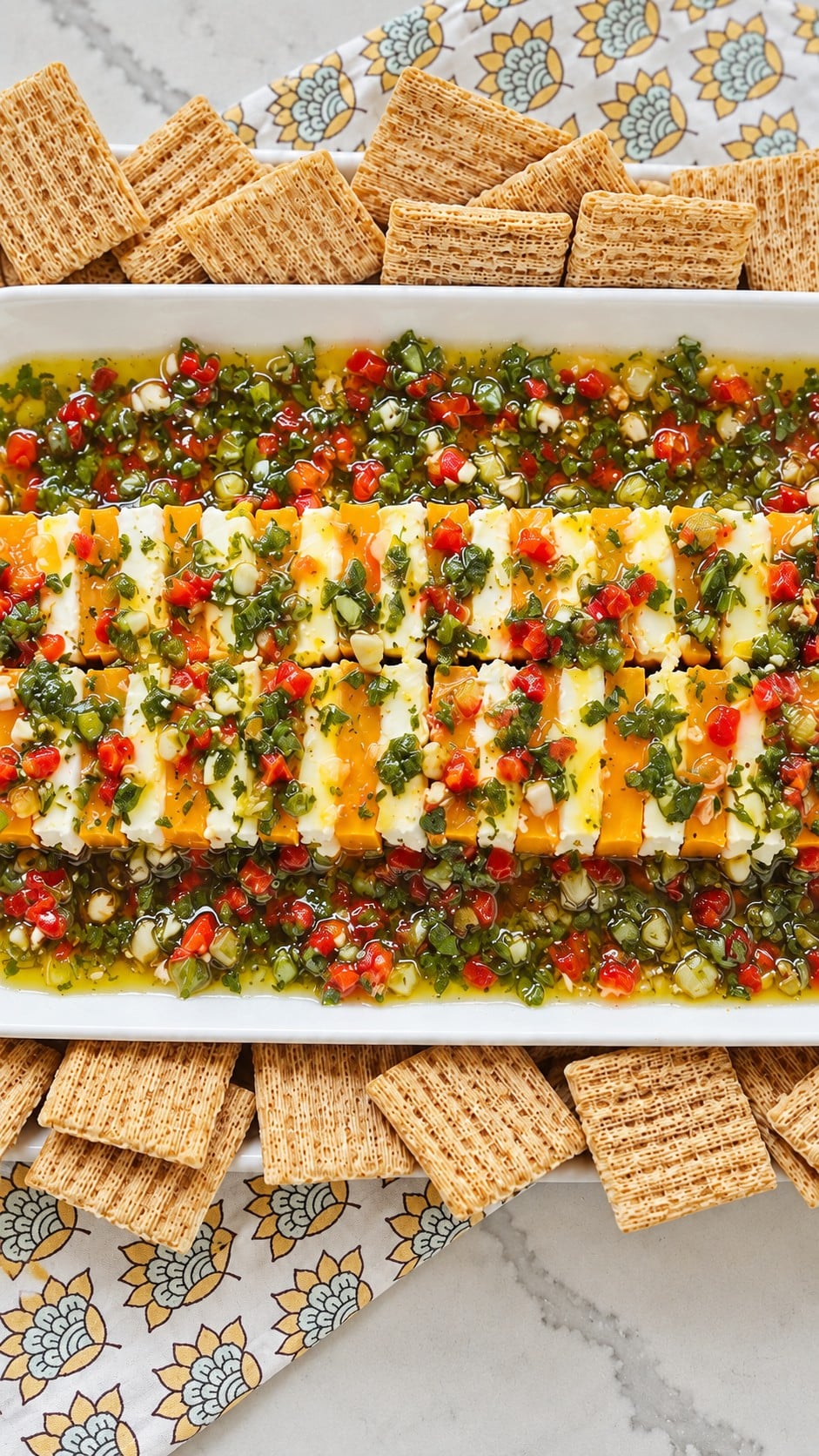 Close-up of alternating cheddar and cream cheese with chopped herbs and red pimentos.