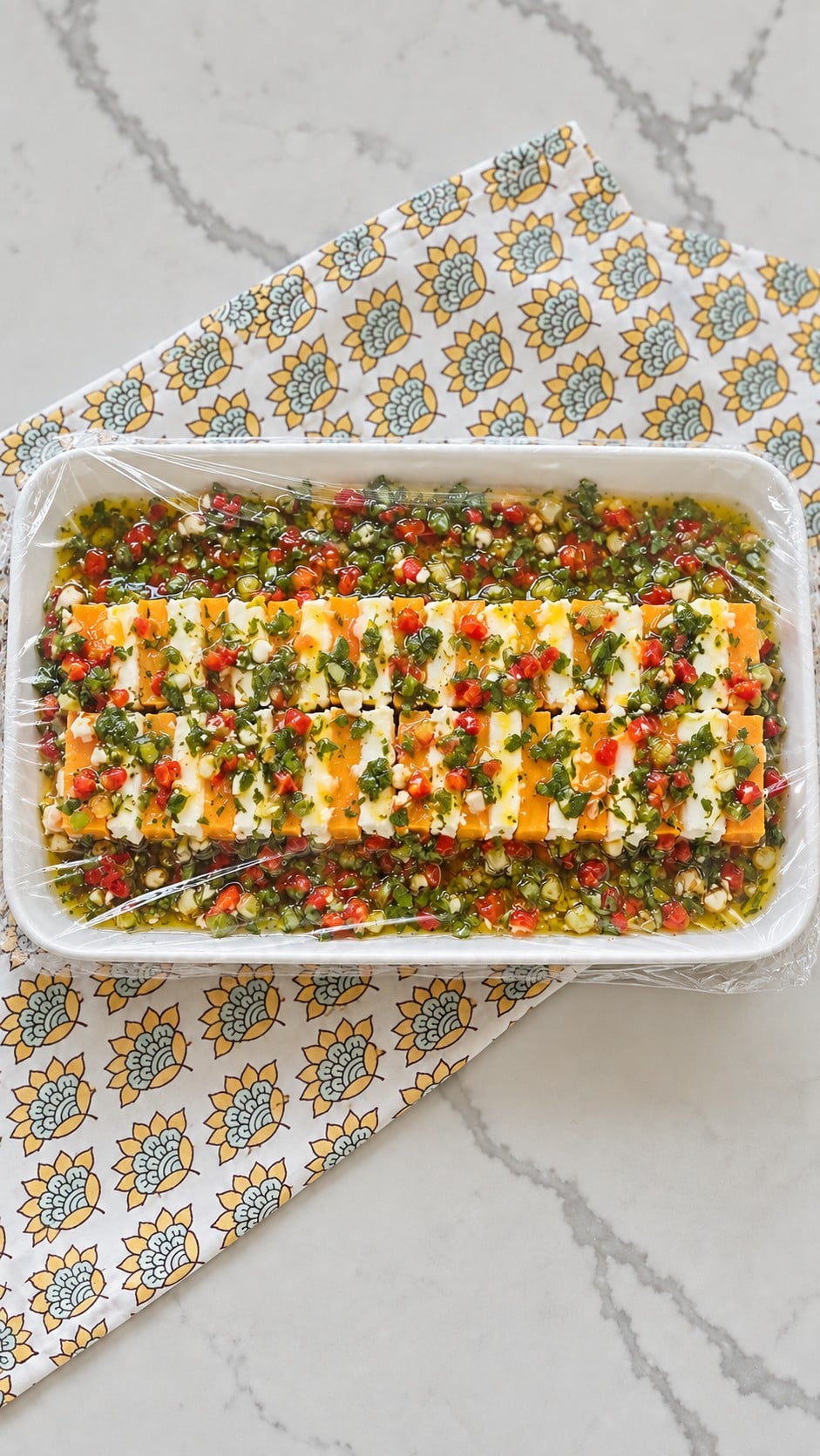 Marinated cheese covered with food wrap for an overnight refrigerator rest.