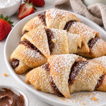 Four golden Nutella crescent rolls dusted with powdered sugar on a white oval platter