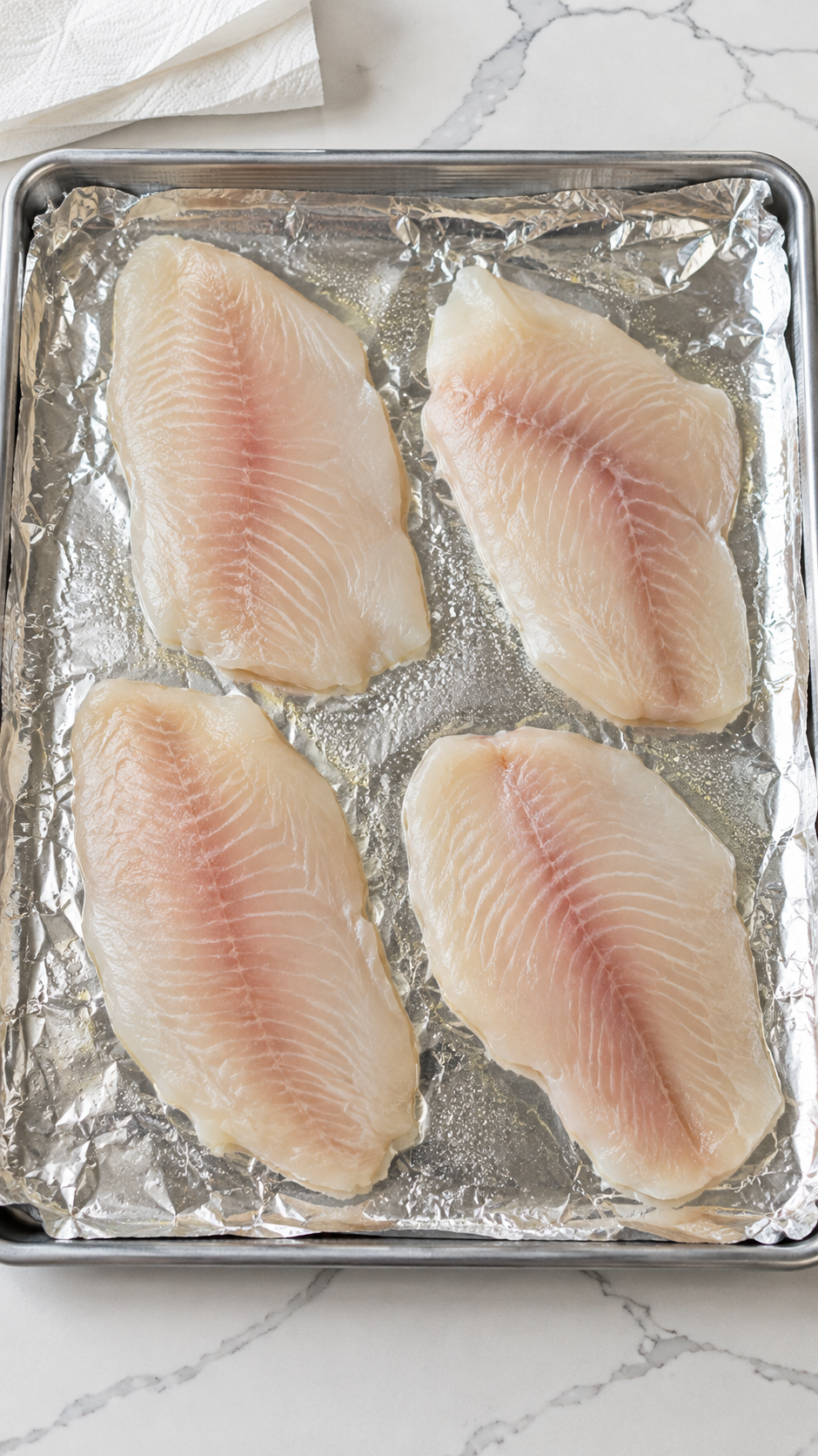 Raw tilapia fillets arranged on a foil-lined baking sheet