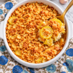 Southern yellow squash casserole with golden crushed Ritz topping in a white round dish and a gold serving spoon