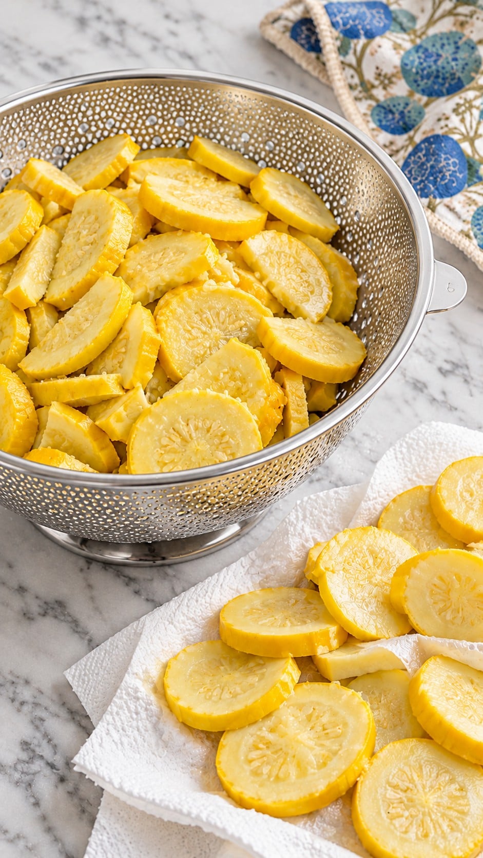 Sliced yellow squash draining in a stainless steel colander before cooking