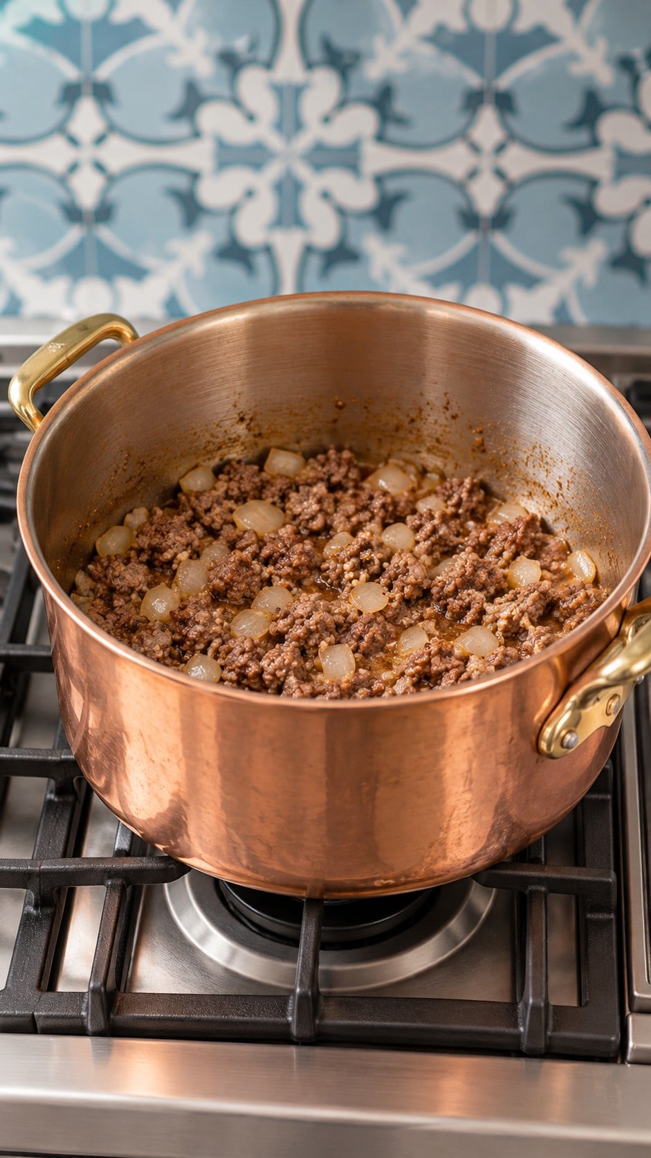 Browned beef and sausage with onion and garlic in a copper and brass soup pot.