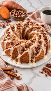 Spiral sweet potato pecan pound cake with thick creamy buttermilk glaze and chopped pecans on a white platter.