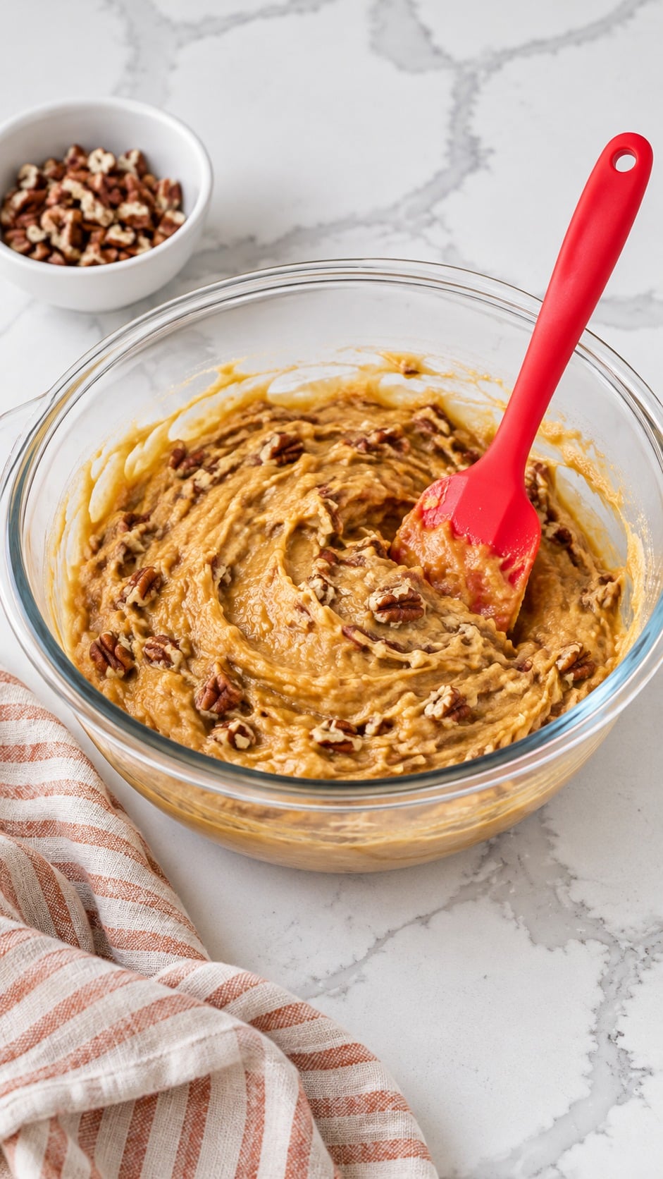 Chopped pecans folded into sweet potato pound cake batter with a red silicone spatula.