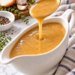 Golden turkey gravy pouring from a gold spoon into a white gravy boat.
